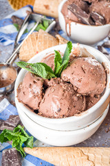 Homemade chocolate ice cream with chocolate pieces and shavings, and ice cream cones. In small white bowls on white grey stone table copy space