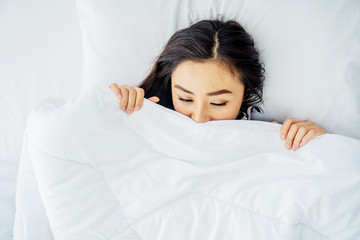 Top view of sleeping asian woman cover face with blanket flat lay. Close-up of young women, sleeping under white blanket and covering half face. Copy space for advertisement.