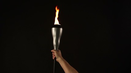 Human hand Lifting and Holding a flaming Torch on a Black Background with flames burning. Stock Video Clip Footage