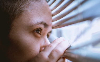 a man looks out the window through the blinds while staying at home during the coronavirus pandemic...