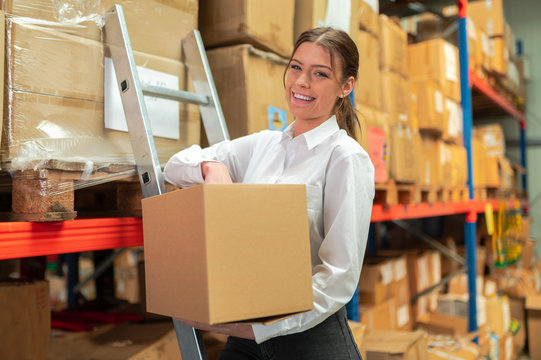 Woman in warehouse is picking up goods in a box