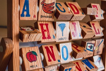 Italian alphabet learning toy for kids, with some red and blue letters and words on it over a wood...