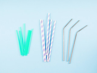 Different material drinking straws on pastel blue background - plastic, paper and eco friendly plastic free stainless steel reusable straws. Flat lay