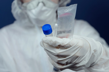 Medical healthcare technologist holding COVID-19 swab collection kit, wearing white PPE protective...