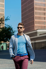 Young bearded man with sunglasses, model of fashion, in urban background wearing casual clothes while walking with hand on pocket