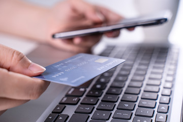 Online paying shopping, electronic payment with credit card, smart phone concept, laptop over white table background with shop cart trolley, close up.