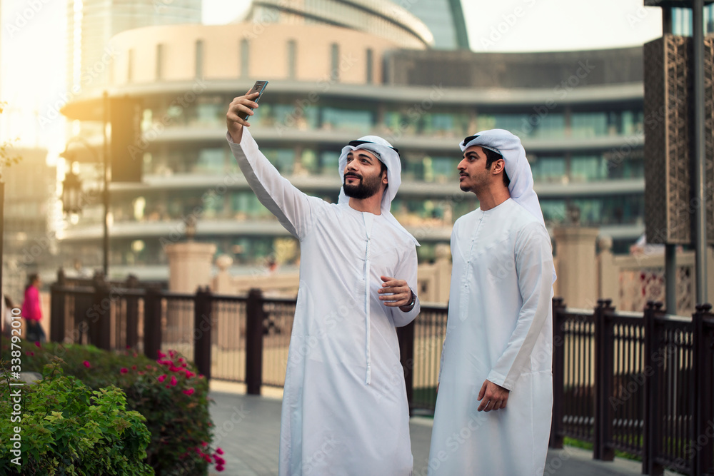 Wall mural two arab young men taking selfie in dubai streets