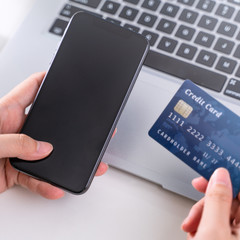 Online paying shopping, electronic payment with credit card, smart phone concept, laptop over white table background with shop cart trolley, close up.