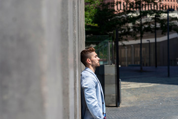 Pensive young bearded man looking away in the street while leaning on a wall outdoors