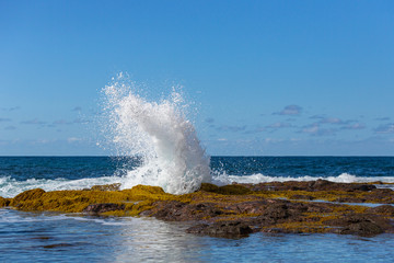 A blue wave breaking into the rocks and making a big splash in Tenerife, Canary Islands, Spain