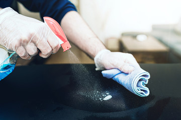 close-up of person wearing disposable one-way gloves using disinfectant spray to clean table...