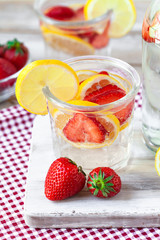 Refreshing homemade lemonade with fresh strawberry, lemon and ice. Healthy cold drink, low calories. Tasty cool summer beverage. Wooden white background, two glasses. Macro, close up