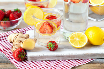 Refreshing homemade sparkling lemonade with fresh strawberry, lemon, ice and ginger. Healthy cold drink, low calories. Tasty cool summer beverage. Wooden white background, red napkin as decor