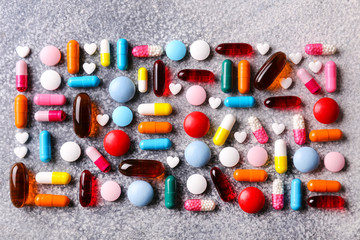 Flat lay composition with bunch of different colorful pills scattered over the concrete table. Pile of opened medication on grey grunged stone textured background. Close up, copy space for text.