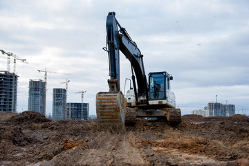 Excavator at building under construction. Backhoe digs the ground for the foundation and for laying sewer pipes. Renovation program. Buildings industry background