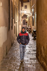 Obraz na płótnie Canvas A young handsome bearded man walking by the streets of Florence at night while looking at the camera