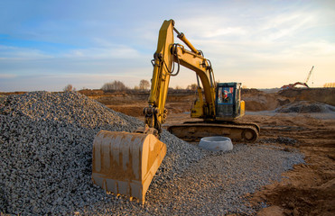 Excavator during earthmoving work at open-pit mining on blue sky background. Loader machine with bucket in sand quarry. Backhoe digging the ground for the foundation and for laying sewer pipes