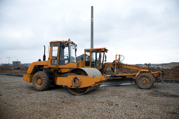 Motor Grader and Soil Compactor at a construction site level the ground and gravel stones for the construction of a new asphalt road. Vibration single-cylinder road roller. Road construction equipment