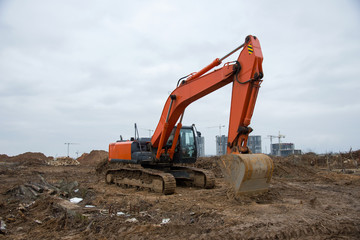 Track-type excavator during earthmoving at construction site. Backhoe digging the ground for the foundation and for laying sewer pipes district heating. Earth-moving heavy equipment