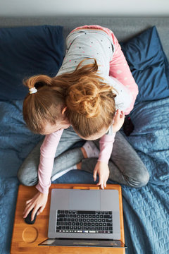 Grandchildren Teenage Girl And Her Younger Sister Talking On Video Call With Granparents On Laptop From Home During COVID-19 Quarantine. Girls Sitting On Bed In Front Of Computer