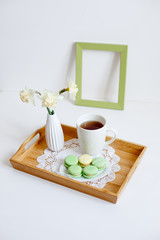 Wooden breakfast tray with a bouquet of spring flowers in bed . Cup of morning tea with macaroons and a flower