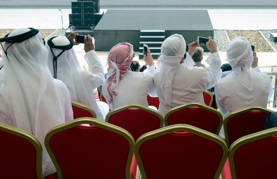 Arabic men in traditional white clothes take pictures with smartphones during an event. Digital world