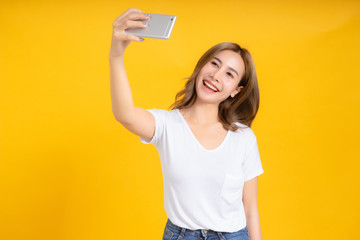 Portrait happy young asian woman selfie with camera smartphone mobile joyful funny positive emotion in white t-shirt, Yellow background isolated studio shot and copy space.