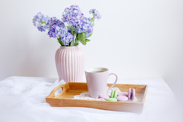 Wooden breakfast tray with a bouquet of spring flowers in bed .a Cup of morning tea with macaroons and a flower