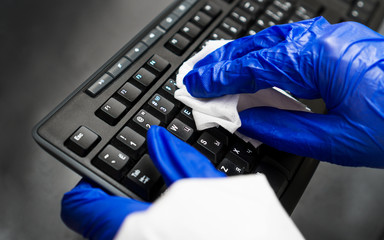 Hand in protective glove with napkin cleaning keyboard. Covid-19 disinfection concept.