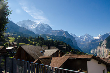 Picturesque Alpine village Wengen, Switzerland. Famous Lauterbrunnen and Staubbach Falls in background. Swiss Alps with snow on top. Switzerland in summer. Alpine landscape