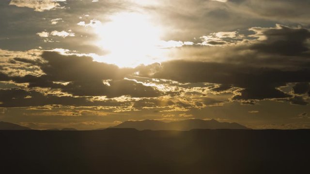 A stunning long-lens sunset timelapse of Canyonlands National Park as seen from Needles Overlook as the sun moves behind dramatic clouds close to the horizon.