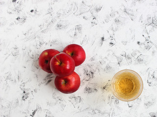 apple juice in a crystal glass and ripe red apples on a white table on a background of a white brick wall.