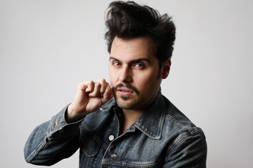 Headshot of serious stylish hipster looks straight with confident expression, wears denim jacket, isolated.