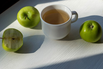 Cup of tea and green apples on a wooden table.