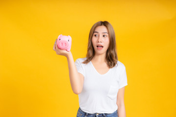 Portrait happy young asian woman holding piggybank saving money for future and business earning income positive emotion in white t-shirt, Yellow background isolated studio shot and copy space.