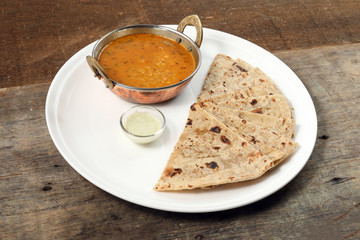 Handmade flat bread chapati and dal tadka fry in brass bowl pan on white plate rustic wooden background