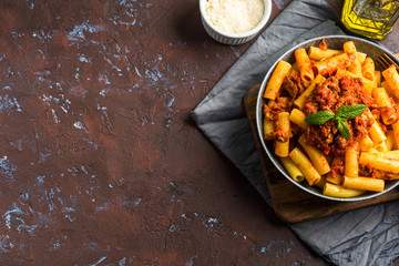 Delicious rigatoni pasta with italian tomato meat ragu sauce served in a pan on dark brown background. Traditional pasta dish concept. Home made lunch