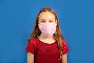 Young long-haired girl in a protective medical mask on a blue background, place for text