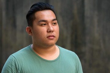 Face of young handsome overweight Asian man thinking outdoors