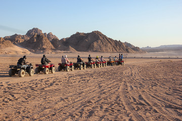Many tourists riding on quad bikes in desert of Egypt near mountains