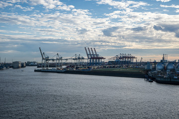 Obraz premium Hamburg container port with some ships loading and cranes transporting container to the freighters at sunset/twilight