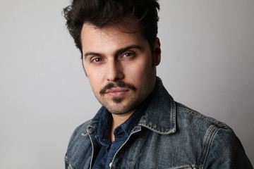 Close-up portrait of serious stylish hipster looks straight with confident expression, wears denim jacket, isolated.