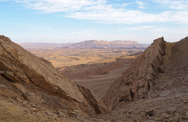 The desert landscape with the big valley, the big rock on foreground, the sandstone and magmatic multicolor rocky mountains, the blue sky with white clouds. 