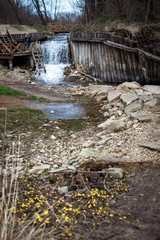 Obraz premium Waterfall near a log wall and a wooden staircase. A spring in Kazan and a font, a stormy river beautifully decorated with wooden bars