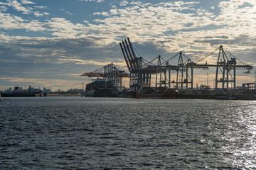 Hamburg container port with some ships loading and cranes transporting container to the freighters at sunset/twilight