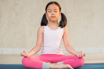 Fototapeta premium calmness and relax, female freedom happiness. home practice room background. little asian girl meditates while practicing yoga. child happiness. toned picture healthy life. yoga concept.