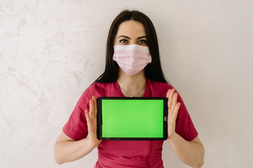 doctor in medical mask holding tablet. green screen