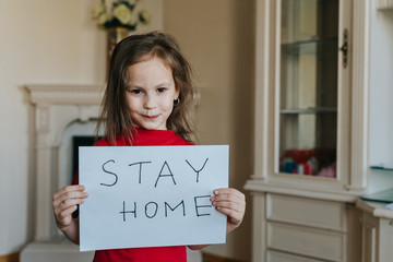 Stay at home concept. Small girl in red T-shirt holding sign saying stay at home for virus protection and take care of their health from COVID-19. Quarantine concept.