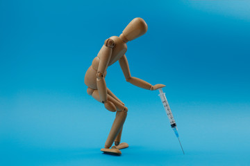 Wooden man figure is in a tired pose the man leans on the syringe as on a walking stick. Concept of fatigue from a long illness and high fever