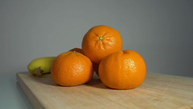 Nutritious Mandarin Oranges On The Wooden Chopping Board With A Piece Of Banana Behind - Closeup Shot